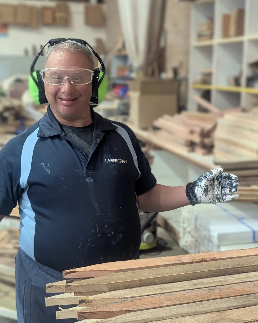 A Lasercraft employee in safety glasses and ear protection standing at the timber racks in the West Gosford workshop, beside a stack of cut survey pegs.